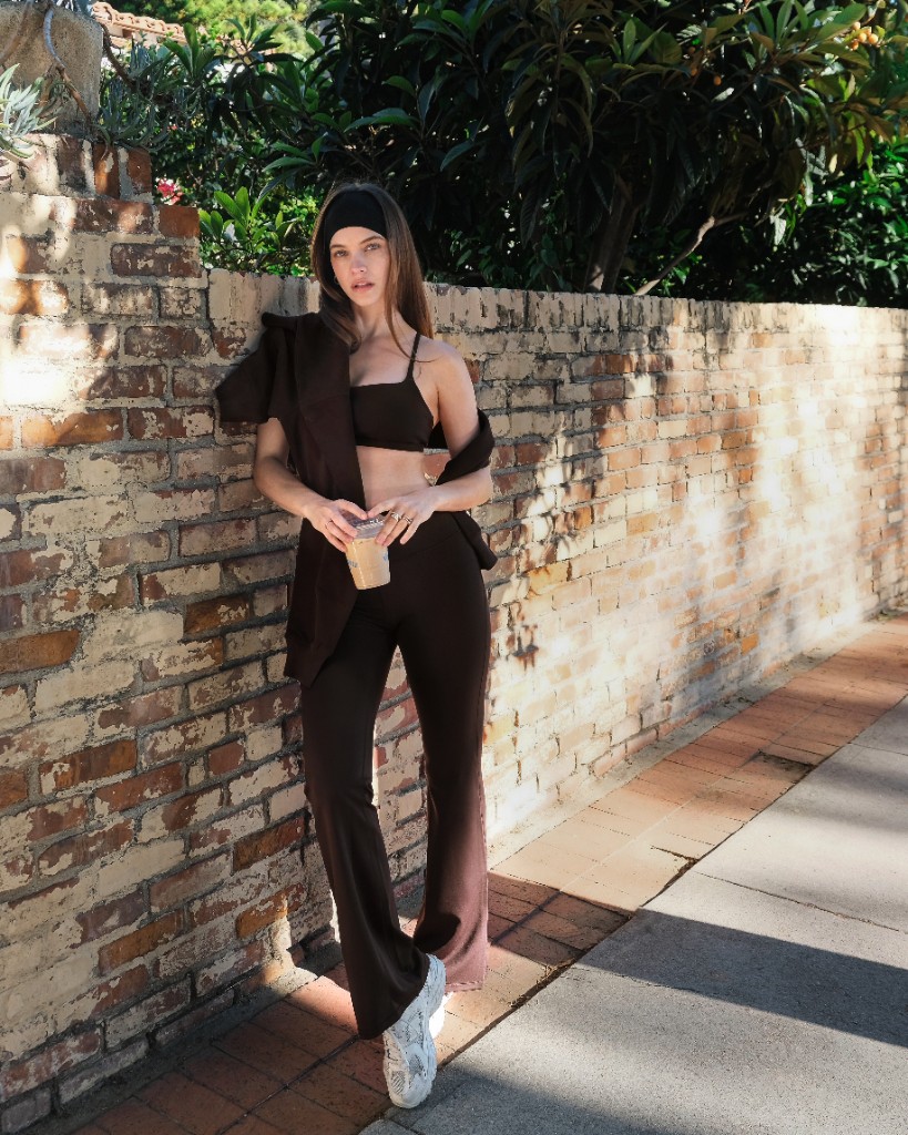 Woman in SilkContour coffee-brown set, iced coffee in hand, brick wall street style